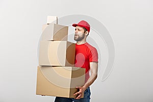 Delivery Concept: Handsome delivery man hold pile cardboard boxes on grey background.