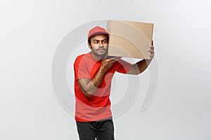 Delivery Concept - Portrait of Curious African American delivery man listen inside a box package. Isolated on Grey