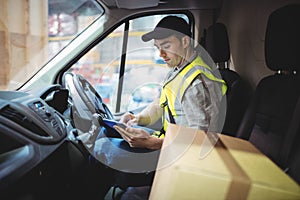 Delivery driver using tablet in van with parcels on seat