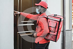 Delivery food man with thermal bag ringing the doorbell while wearing safety mask - Focus on face