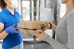 Delivery girl in mask giving pizza boxes to woman