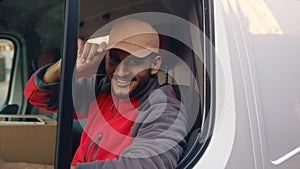 Delivery guy wearing red uniform sitting in the white van and tipping his cap