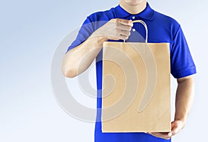 Delivery man in blue uniform and holding paper bag with delivering package on gray background. Concept fast food delivery service