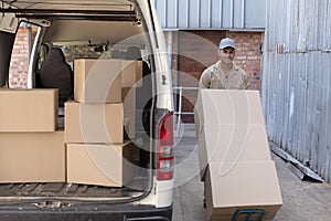 Delivery man carrying cardboard boxes on trolley near van outside the warehouse