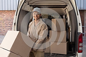 Delivery man carrying cardboard boxes on trolley near van outside the warehouse