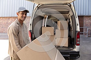 Delivery man carrying cardboard boxes on trolley near van outside the warehouse