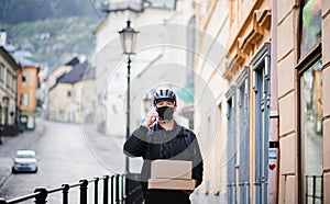 Delivery man courier with face mask and smartphone delivering parcel box in town.