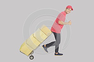 Delivery man or courier pushing hand truck with stack of boxes and showing like