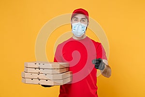 Delivery man employee in red cap blank t-shirt uniform mask gloves give food order pizza boxes isolated on yellow