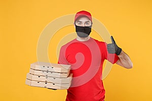 Delivery man employee in red cap t-shirt uniform black mask gloves give food order pizza boxes isolated on yellow