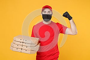 Delivery man employee in red cap t-shirt uniform black mask gloves give food order pizza boxes isolated on yellow