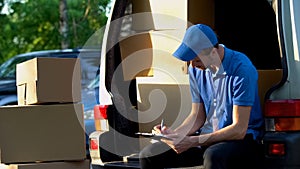 Delivery man filling transportation documents, sitting near van trunk, duties