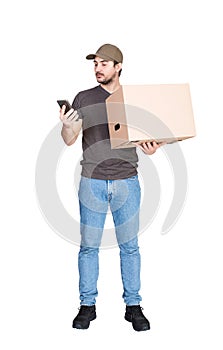 Delivery man, full length portrait, holding a cardboard parcel box while using his smartphone, isolated on white. Modern courier