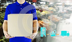 Delivery man hand holding paper box package in blue uniform and icon media symbol on grocery background. Delivery service