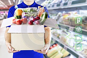 Delivery man hand holding paper box package in blue uniform and icon media symbol on grocery background. Delivery service