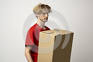 Delivery man holding a cardboard boxes and smiling while standing against white background. Courier holding a cardboard