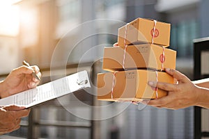 Delivery man holding parcel boxes while a man is signing documents in morning background