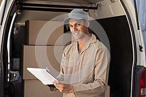 Delivery man looking at camera while writing on clipboard near van outside the warehouse