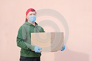 Delivery man in medical mask and gloves holding and carrying a cardbox