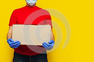 Delivery man in medical mask holding a cardbox on Yellow background