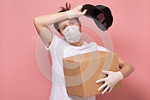 Delivery man in medical mask holding and carrying a cardbox wiping the sweat