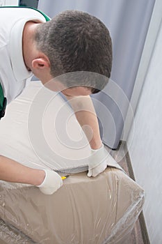 The delivery man in protective gloves, opens the furniture from the box, cuts the dense polyethylene