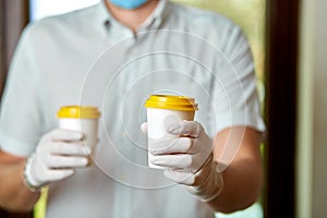 Delivery man in protective mask and gloves, employee hold takeaway cup of coffee.