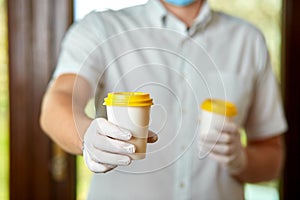 Delivery man in protective mask and gloves, employee hold takeaway cup of coffee.