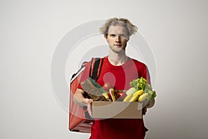 Delivery man in red uniform delivering food, groceries, vegetables, drinks in a paper box to a client at home. Online