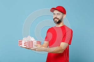 Delivery man in red uniform hold present box isolated on blue wall background, studio portrait. Professional male
