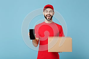 Delivery man in red uniform isolated on blue background, studio portrait. Male employee in cap t-shirt print working as