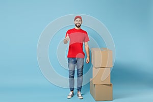 Delivery man in red uniform isolated on blue background, studio portrait. Male employee in cap t-shirt print working as