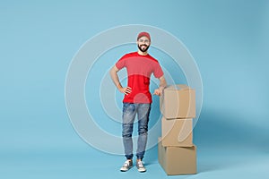 Delivery man in red uniform isolated on blue background, studio portrait. Male employee in cap t-shirt print working as