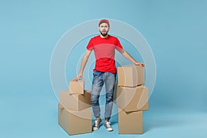 Delivery man in red uniform isolated on blue background, studio portrait. Male employee in cap t-shirt print working as