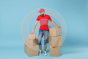 Delivery man in red uniform isolated on blue background, studio portrait. Male employee in cap t-shirt print working as