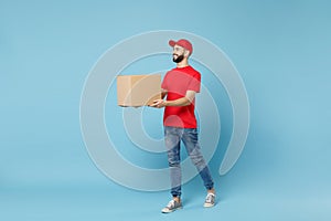 Delivery man in red uniform isolated on blue background, studio portrait. Male employee in cap t-shirt print working as