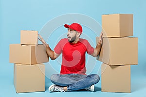 Delivery man in red uniform isolated on blue background, studio portrait. Male employee in cap t-shirt print working as