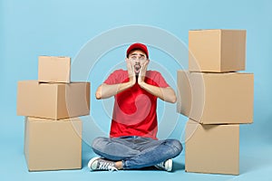 Delivery man in red uniform isolated on blue background, studio portrait. Male employee in cap t-shirt print working as