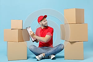 Delivery man in red uniform isolated on blue background, studio portrait. Male employee in cap t-shirt print working as