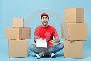 Delivery man in red uniform isolated on blue background, studio portrait. Male employee in cap t-shirt print working as