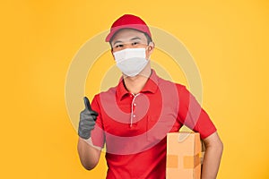 Delivery man in red uniform He was wearing a mask and black gloves holding a brown cardboard box and thumbs up