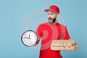 Delivery man in red workwear giving food order pizza boxes isolated on blue background, studio portrait. Professional