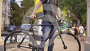 Delivery man standing with bike and yellow bag in medical mask
