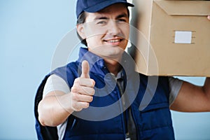 Delivery man in uniform is holding parcel cardboard box over blue background.