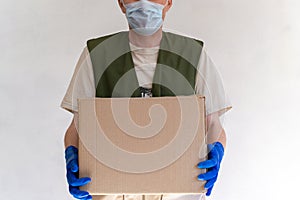 Delivery man in uniform. Holds a cardboard box in medical protective gloves and a mask. Fast and free delivery of transport.