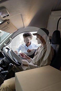 Delivery man and warehouse manager discussing over clipboard outside the warehouse