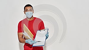 Delivery man wearing face mask and protective gloves holding parcels and envelopes, showing form for signing on