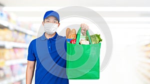 Delivery man wearing medical mask holding grocery shopping bag in supermarket