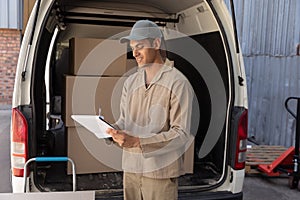 Delivery man writing on clipboard near van outside the warehouse