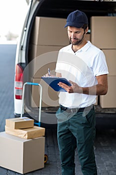 Delivery man writing on clipboard while standing next to his van